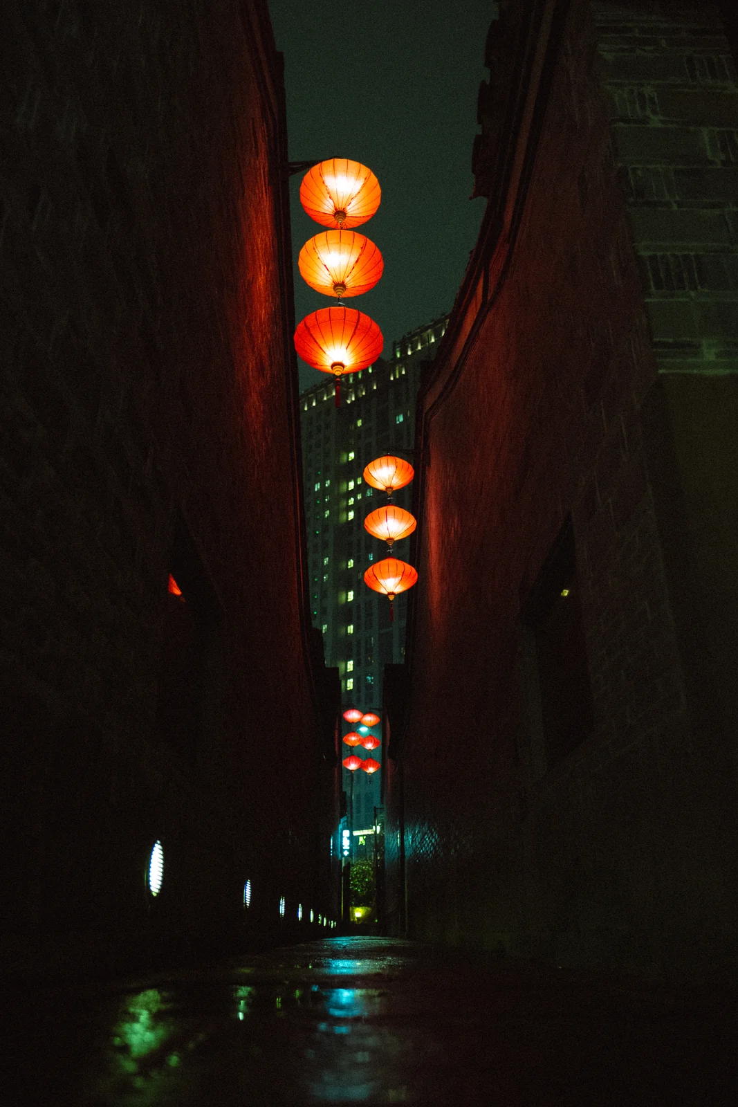 A narrow night alley strung with red paper lanterns over wet ground, graded with GX-05 Back Alley