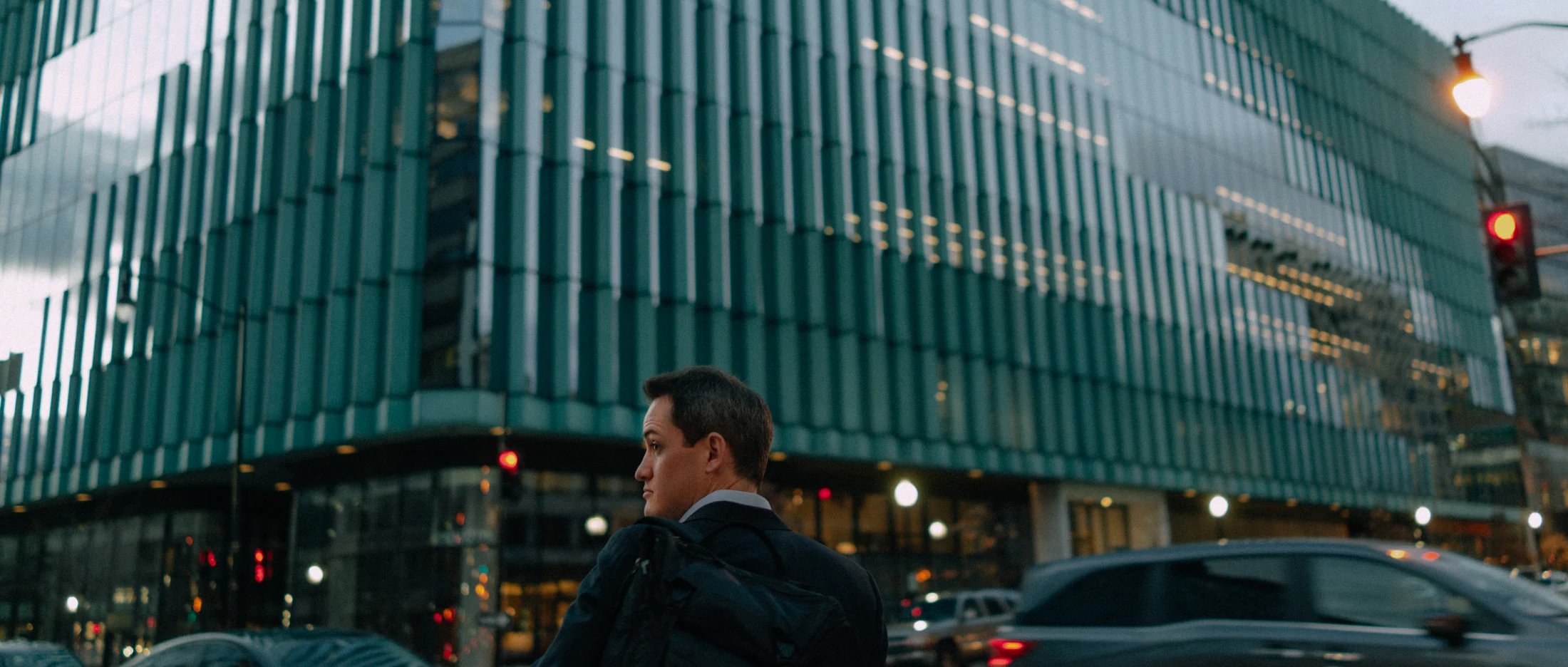 A man in a suit on a corner in front of a green glass office building, graded with GX-05 CineGold