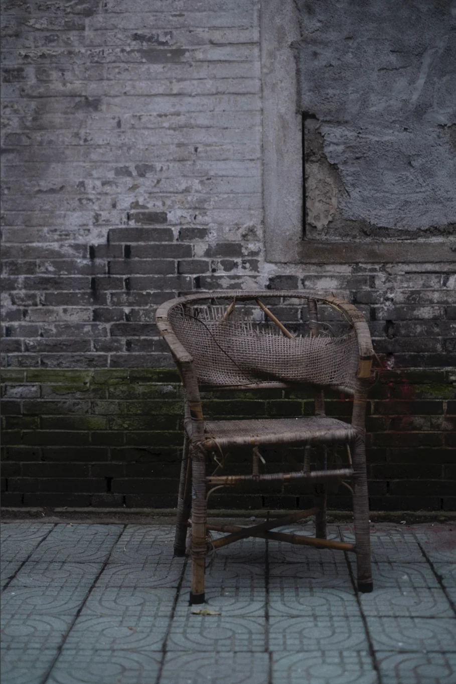 A worn rattan chair against a grey brick wall on a paved street, graded with GX-02 Chlorine