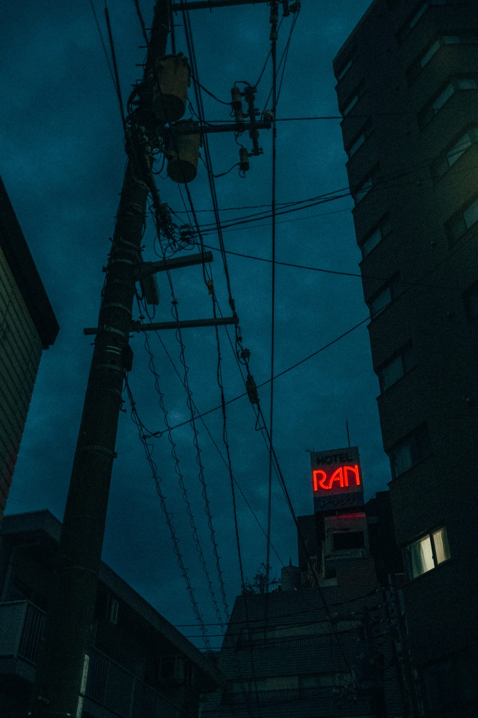 Overhead power lines and a red HOTEL RAN neon sign against a deep blue night sky