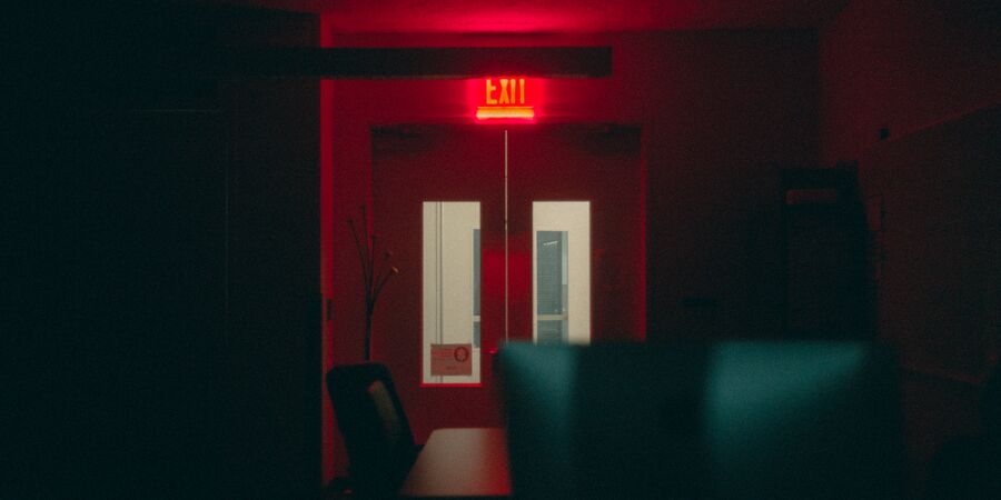 A dim red-lit interior with a glowing EXIT sign above double doors